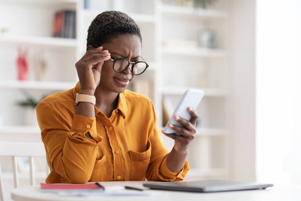 Confused black woman looking at smartphone screen, touching glasses - Foto, Imagen