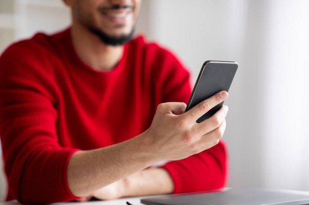 Cropped smiling young islamic man with beard typing on smartphone in home office interior - Fotoğraf, Görsel