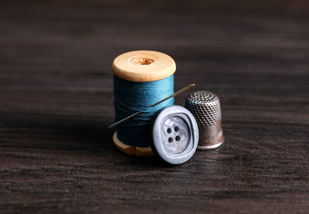 Spool of light blue thread with needle, button and thimble on wooden table. Sewing accessories - Foto, afbeelding