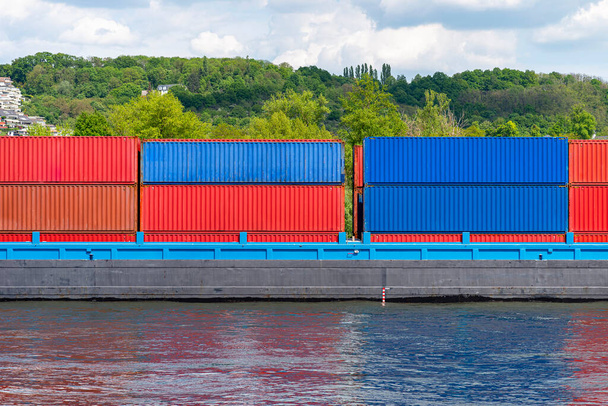 A barge carrying many containers on the Rhine in western Germany, trees and buildings in the background. - Photo, image