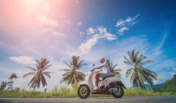 Stylish young man rides a motorbike on the road near the sea and palm trees - Foto, Bild