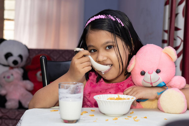 Una bambina indiana mangia cereali con latte dal viso sorridente e guarda la macchina fotografica - Foto, immagini