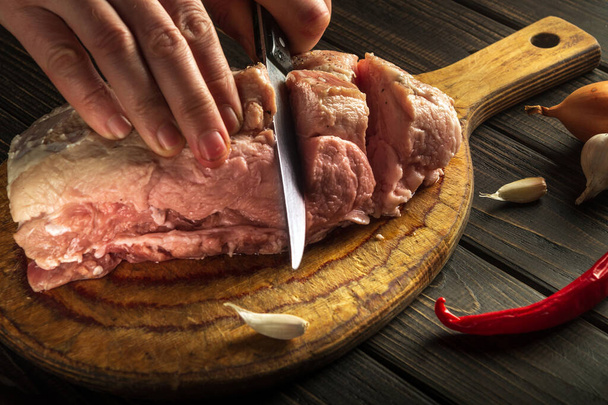 Die Hände eines Kochs mit einem Messer in der Küche schneiden rohes Fleisch zum Grillen. Köstliches Essen für das Restaurant zubereiten - Foto, Bild