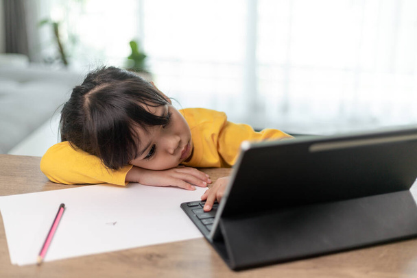 Little Asian girl sitting alone and looking out with a bored face, Preschool child laying head down on the table with sad  bored with homework, spoiled child - Foto, Imagen