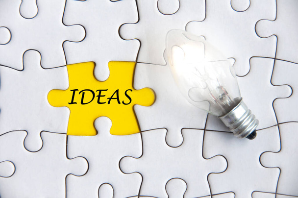 Ideas text on missing jigsaw puzzle with light bulb background. - Фото, изображение