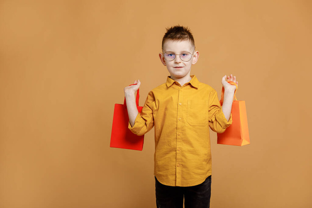 Shopping on black friday. Little boy holding shopping bags on yellow background. Shopper with many colored paper bags. Holidays sales and discounts. Cyber monday. High quality photo. - Foto, Imagen