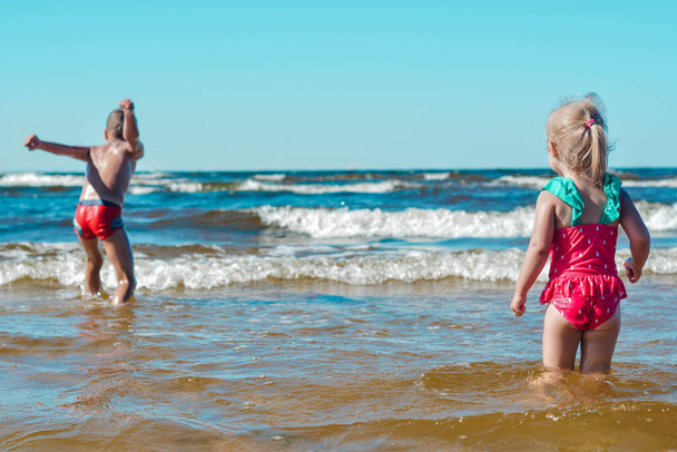 Chica y niño de apariencia europea divirtiéndose en el agua en la playa y salpicaduras - Foto, Imagen
