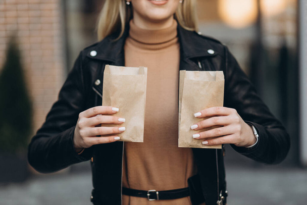 Blondynka trzymająca paczkę rogalików na tle centrum handlowego. Piękna dziewczyna w centrum miasta. Croissant w opakowaniu. - Zdjęcie, obraz