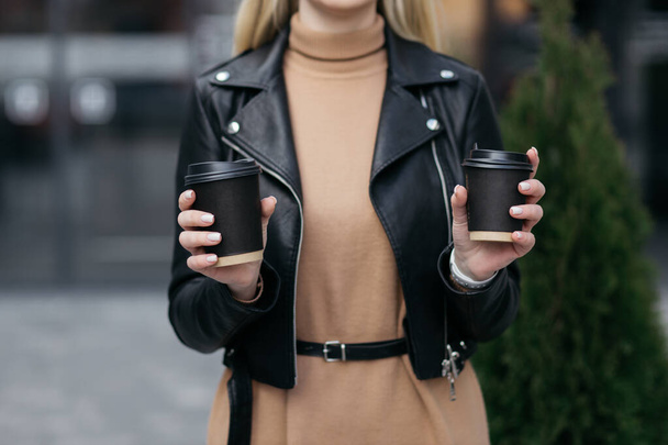 Girl is holding two paper cup next to her. Paper cup of coffee in woman's hand on shop background. Hot drink. Hand holds a paper cup of coffee. Coffee. - Photo, Image