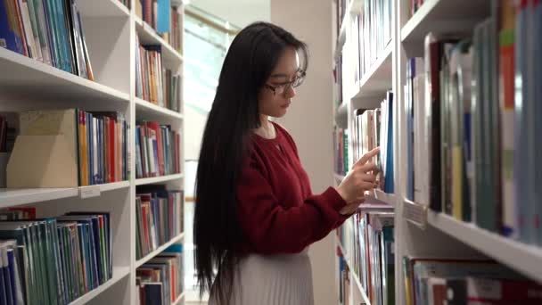 Asijské studentky vyzvednout knihu z police, zatímco stojí mezi knihovnami - Záběry, video