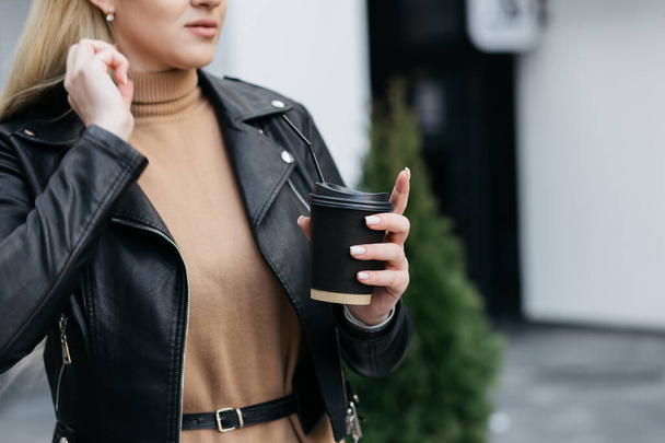 Girl holding a cardboard cup. Paper coffee cup in a woman hand on store background. Hot drink. Hand holding paper cup of coffee. Paper coffee cup. - Foto, Imagen