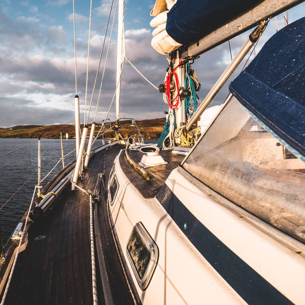 Sloop megbütykölte a modern jachtot fából készült teak fedélzettel, amely naplementekor az Islay-sziget partjainál vitorlázott. Belső Hebridák, Skócia, Egyesült Királyság. Sport és rekreáció, úticélok, nevezetességek, közlekedés - Fotó, kép