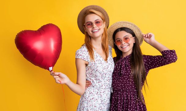 glad mom and daughter hold love heart balloon on yellow background - Фото, изображение