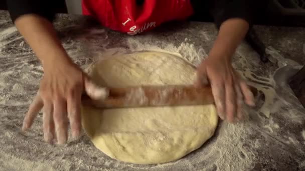 Chef rocks dough with rolling pin on kitchen table against background of flour - Metraje, vídeo