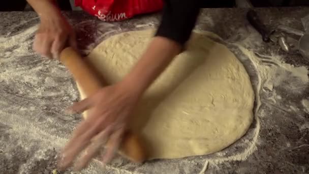 Chef rocks dough with rolling pin on kitchen table against background of flour - 映像、動画