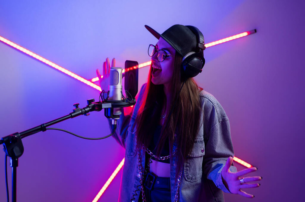 Красивая стильная девушка поет в микрофон в студии звукозаписи  - Фото, изображение