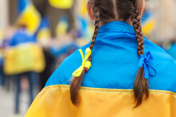 Rally support Ukraine in Europe. Ukrainian Flag on Shoulders of Girl with blue yellow ribbons on flags background. - Фото, зображення