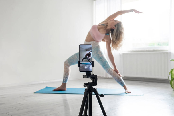 woman practicing yoga poses stretching in front of phone camera sport blogger teacher yoga online - Фото, изображение