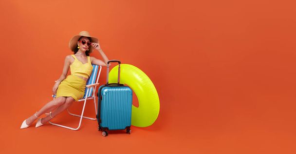 Beautiful woman relax sitting on a beach chair with suitcase and rubber ring in studio summer orange background with copy space. - Fotoğraf, Görsel