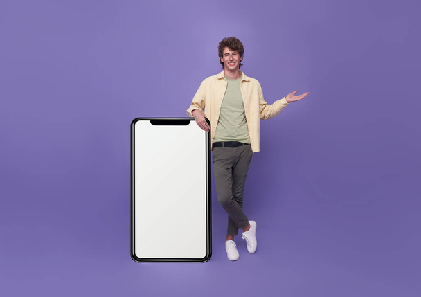 Young handsome man standing with mockup big Smartphone blank white screen isolated on purple studio background. - Fotografie, Obrázek