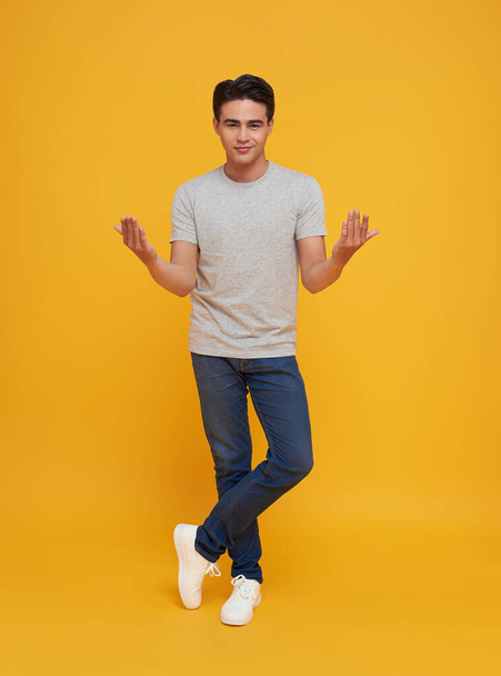 Portrait of surprised smiling young handsome Asian man looking camera and presenting with open palms gesture in isolated studio yellow background. - Foto, Bild