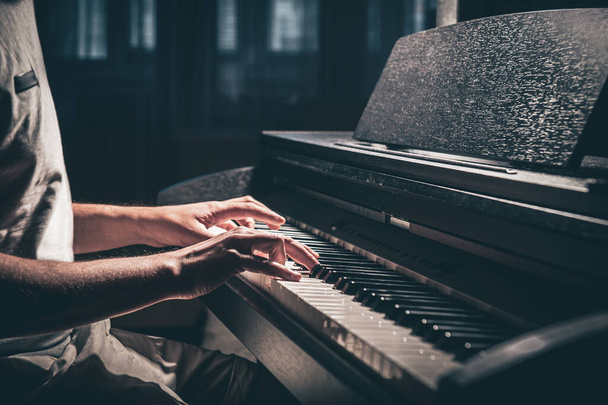 Ένας άντρας παίζει ηλεκτρονικό πιάνο σε σκοτεινό δωμάτιο.. - Φωτογραφία, εικόνα