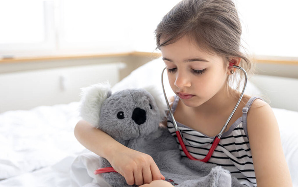A little girl plays doctor with her favorite soft toy. - Foto, imagen