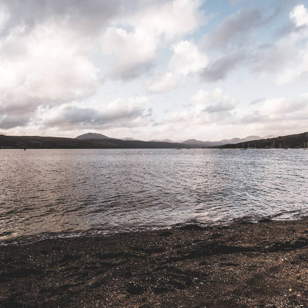 Skaliste jezioro brzeg pod burzliwym wieczornym niebem po deszczu. Dramatyczny zachmurzony zachód słońca. Gare Loch, Rhu, Szkocja, Wielka Brytania. Cele podróży, wakacje, koncepcje spędzania wolnego czasu - Zdjęcie, obraz