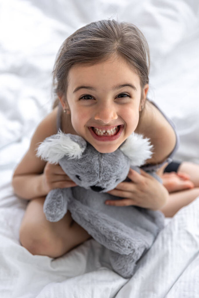 Happy little girl with soft toy koala in bed. - Фото, изображение