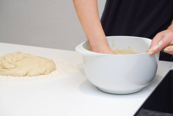 DIY home cooking concept. A young woman works with yeast dough in a modern kitchen. A young woman is kneading a dough, engaged in cooking homemade bakery. - Photo, Image