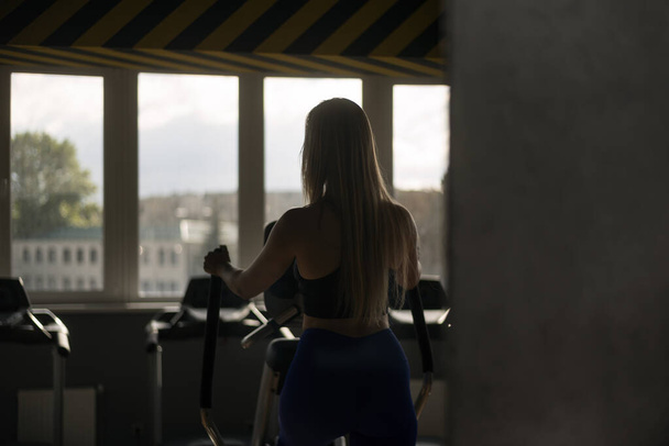 Back view portrait of girl with long hair in the gym training on the orbitrek Elliptical Trainer - Zdjęcie, obraz