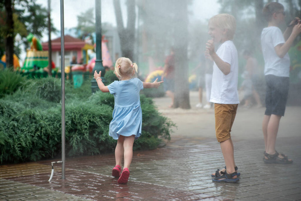 Lapset leikkivät vesisuihkujen alla kesäpuistossa. Tuuli kuumana päivänä. Leikkikenttä - Valokuva, kuva