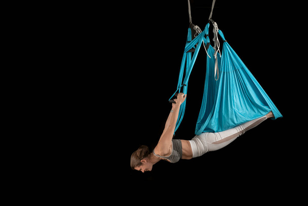 Ganzkörperansicht der Sportlerin übt Aero-Fly-Yoga-Position, während sie kopfüber hängt. Schwarzer Hintergrund. - Foto, Bild
