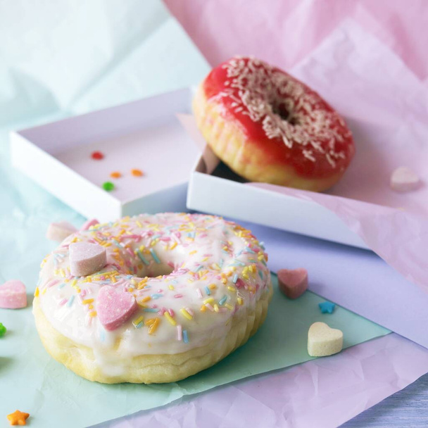 Freshly baked donuts glazed with various pink shades and sprinkled with caramel hearts, lilac shade wrapping paper on the table, Donut Day  - Photo, Image