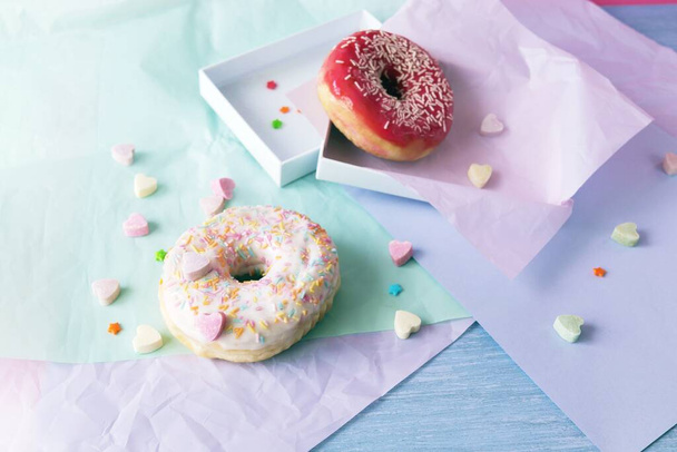 Freshly baked donuts glazed with various pink shades and sprinkled with caramel hearts, lilac shade wrapping paper on the table, Donut Day  - Foto, imagen