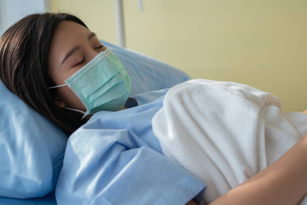 Surullinen aasialainen potilas nainen makaa sairaalassa ja yllään kasvonaamio suojella sepelvaltimovirus. Terveydenhuollon, karanteenikoronaviruksen (COVID-19) ja sairausvakuutuksen käsite. - Valokuva, kuva
