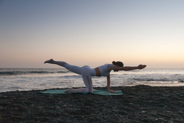 Здоровий з концепцією йоги. Приваблива молода жінка практикує йогу на пляжі під час заходу сонця. Зручно і розслабитися
. - Фото, зображення