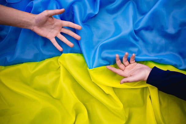 Las manos se extienden entre sí en el contexto de la bandera de Ucrania. - Foto, imagen