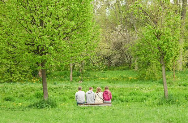 Quatre personnes s'assoient sur un banc dans le parc. - Photo, image