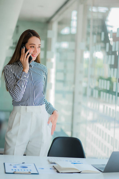 Νεαρή Ασιάτισσα επιχειρηματίας μιλάει σε ένα κινητό τηλέφωνο για οικονομικούς λογαριασμούς στο γραφείο, φωτογραφία πορτραίτου - Φωτογραφία, εικόνα
