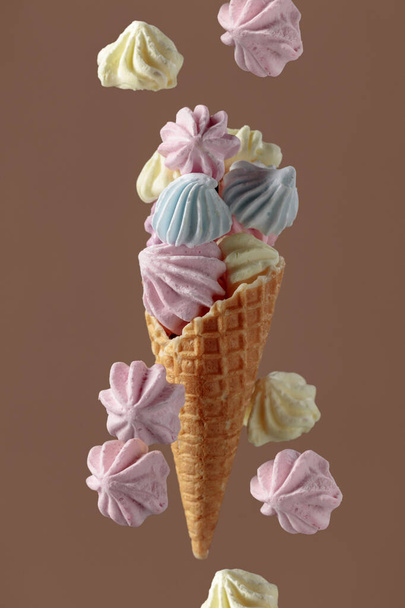 Homemade colorful meringue in a waffle cone on a brown background. - Zdjęcie, obraz
