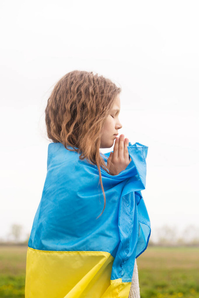 A little girl with the flag of Ukraine prays for the victory of her country - 写真・画像