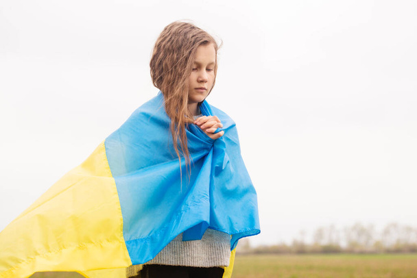 Ein kleines Mädchen mit der Fahne der Ukraine betet für den Sieg ihres Landes - Foto, Bild
