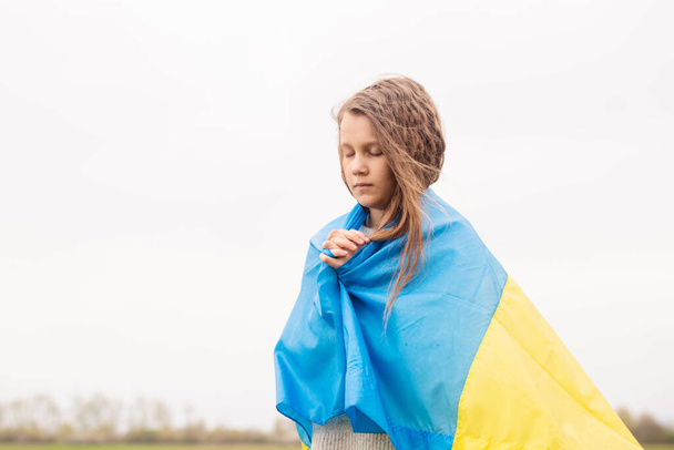 Una niña con la bandera de Ucrania reza por la victoria de su país - Foto, imagen