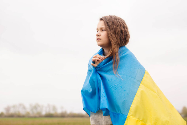 Una bambina con la bandiera dell'Ucraina prega per la vittoria del suo paese - Foto, immagini