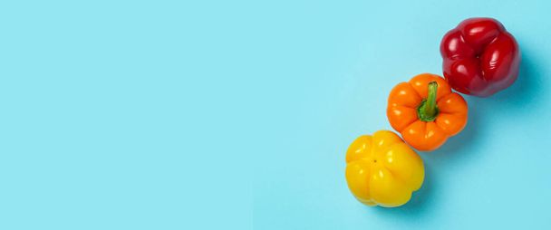 Three fresh bright sweet peppers on a blue background. Top view, flat lay. Banner. - Foto, afbeelding