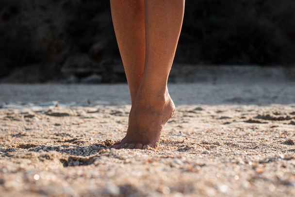 Female bare feet stand on a sandy beach on a summer day.  - Foto, imagen