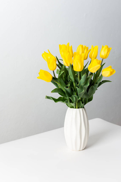 Beautiful spring bouquet of yellow tulips in a white vase on a white table, festive bouquet for birthday or holiday - Zdjęcie, obraz