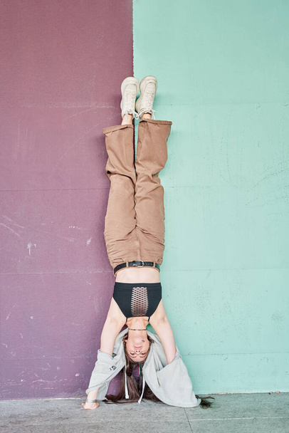 Longitud completa mujer poderosa en ropa casual realizar handstand cerca de la pared colorida - Foto, imagen