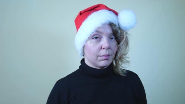 Söpön 40-vuotiaan naisen muotokuva punaisessa uudenvuoden hatussa ja mustassa puserossa. Uudenvuodenloma. Hyvää joulua. Hidasliikkeinen muotokuva - Materiaali, video